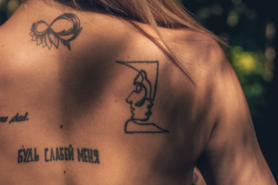 Close-up of artistic tattoos on a woman's back, captured outdoors with natural light.